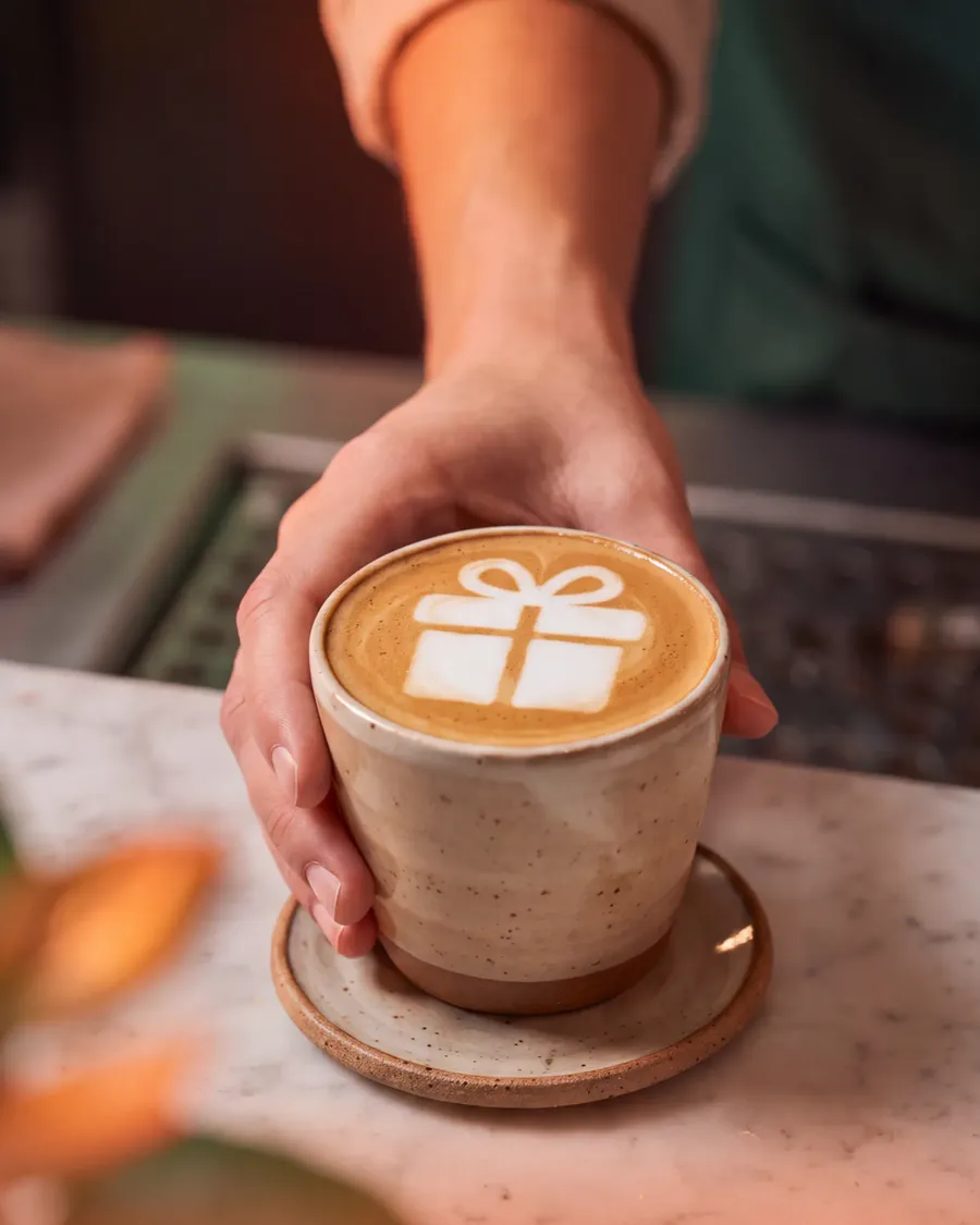 A latte with a gift box drawn in the foam, handed over the counter
